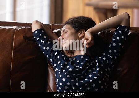 Glückliche, ruhige Lateinerin, die sich auf dem Ledersofa ausruht und Komfort genießt Stockfoto
