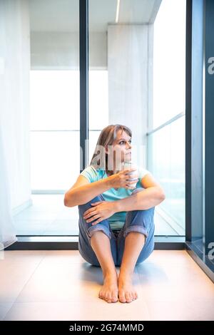Frau mittleren Alters, die sich zu Hause ausruhte und Kaffee trank Stockfoto