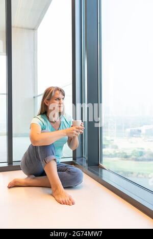 Frau mittleren Alters, die sich zu Hause ausruhte und Kaffee trank Stockfoto