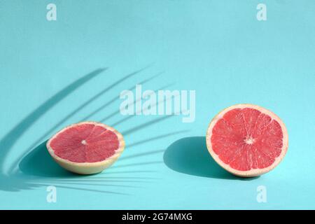Sommerstill-Leben mit zwei geschnittenen Grapefruits mit Palmen Blätter harten Schatten. Auf blauem Hintergrund. Stockfoto
