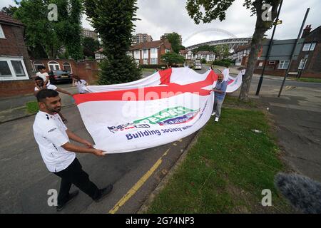 Anwohner tragen eine offizielle Flagge des riesigen England Nationwide Respect-Wahlkampfes von Neeld Crescent in Brent, wo Raheem Sterling aufgewachsen ist, bis zum Wembley-Stadion, bevor die englische Fußballmannschaft beim UEFA Euro 2020-Finale spielt. Bilddatum: Sonntag, 11. Juli 2021. Stockfoto