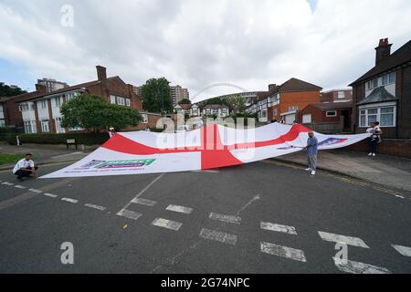 Anwohner tragen eine offizielle Flagge des riesigen England Nationwide Respect-Wahlkampfes von Neeld Crescent in Brent, wo Raheem Sterling aufgewachsen ist, bis zum Wembley-Stadion, bevor die englische Fußballmannschaft beim UEFA Euro 2020-Finale spielt. Bilddatum: Sonntag, 11. Juli 2021. Stockfoto