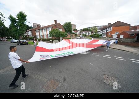 Anwohner tragen eine offizielle Flagge des riesigen England Nationwide Respect-Wahlkampfes von Neeld Crescent in Brent, wo Raheem Sterling aufgewachsen ist, bis zum Wembley-Stadion, bevor die englische Fußballmannschaft beim UEFA Euro 2020-Finale spielt. Bilddatum: Sonntag, 11. Juli 2021. Stockfoto