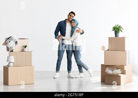 Junges muslimisches Paar zieht in eine neue Wohnung, umarmt und lächelt Stockfoto