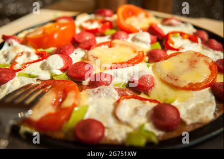 Rührei mit Würstchen, Tomaten, Pfeffer und Grünpflanzen in der Pfanne Stockfoto