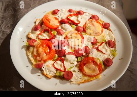 Rührei mit Würstchen, Tomaten, Pfeffer und Grünpflanzen in der Pfanne Stockfoto
