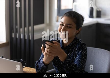 Glücklicher indischer Mitarbeiter, der die App auf dem Smartphone verwendet und im Chat eine SMS schreibt Stockfoto