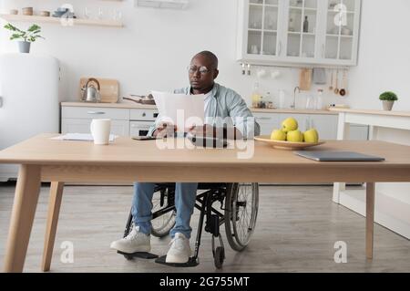 afroamerikanischer Freiberufler, der am Computer schreibt, Papierkram mit Dokumenten auf dem Tisch Stockfoto