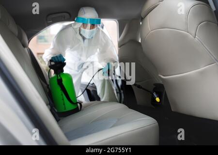 Arbeiter in Gefahrgut Anzug mit chemischen Alkohol Spray Reinigung im Auto zu desinfizieren Stockfoto