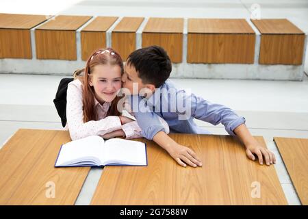 Konzept der ersten Gefühle, Kuss, Schulliebe. Junge küsst Mädchen, Teenager ist sehr glücklich und überrascht, Kindheit, Schulleben, Lebensstil Stockfoto