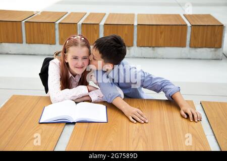 Konzept der ersten Gefühle, ersten Kuss, Schulliebe. Junge küsst Mädchen, Teenager ist sehr glücklich und überrascht, Kindheit, Schulleben, Lebensstil Stockfoto