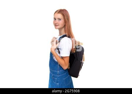 Mädchen Teenager 11 Jahre alt Schulmädchen Blick auf Kamera mit Lächeln auf weißem Hintergrund mit Rucksack. In Denim-Kleid gekleidet, Platz kopieren Stockfoto