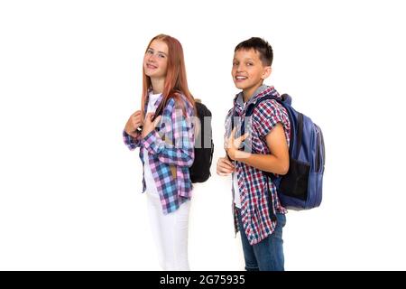 Junge und Mädchen Teenager 11 Jahre alt Schuljunge und Schülerin Blick auf die Kamera auf weißem Hintergrund mit Rucksäcken und lächelnd. In kariertes Hemd gekleidet, Stockfoto