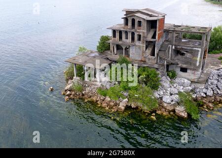 Luftaufnahme einer großen verlassenen Ruinen, Haus, Hotel, die auf einer kleinen Insel mit einer Brücke in der Nähe von Shkodra zerfallen. Albanien, Balkan, Europa Stockfoto