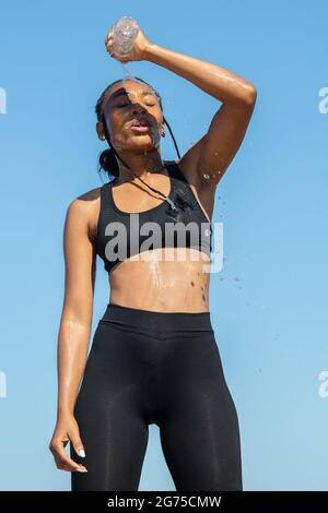 Afro-amerikanerin erfrischt ihren Körper und gießt Wasser auf sich selbst: Bewegung und gesundes Lifestyle-Konzept. Stockfoto