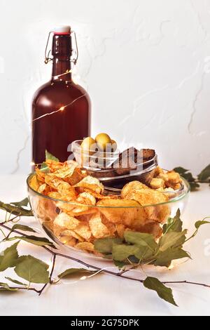 Sommer, Lebensmittelzusammensetzung mit Flasche mit hausgemachtem, natürlichem Bier, salzige Snacks: Roggencracker, Weizencracker, Kartoffelchips mit Gewürzen und grüner Olive Stockfoto