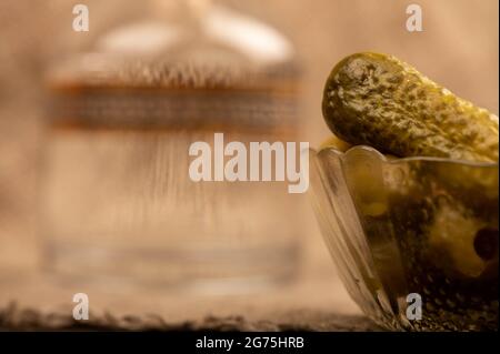 Eine Glasdekanter mit Wodka, ein Glas Wodka und eingelegte Gurken auf einem Hintergrund aus homespun Stoff mit einer rauen Textur. Nahaufnahme Selektiver Fokus Stockfoto