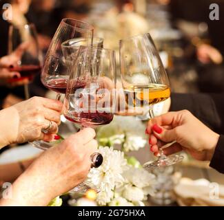 Eine Gruppe anonymer Freunde von Pflanzen klirren Gläser mit Wein, während sie sich am Tisch mit köstlichen Gerichten und Blumenschmuck während des Hausessens treffen Stockfoto