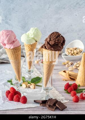 Close-up-Zapfen mit Kugeln aus köstlichem Himbeer-, Kirsch-, Pistazien- und Schokoladeneis.Holzhintergrund mit köstlichem Eis und verschiedenen Stockfoto