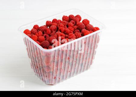 Frische rote Himbeeren in einer Plastikbox auf weißem Holztisch. Stockfoto