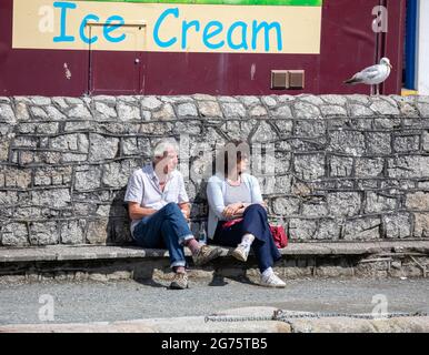 Ein Paar sitzt und entspannt an einer Wand in Porthleven, Cornwall, Großbritannien Stockfoto