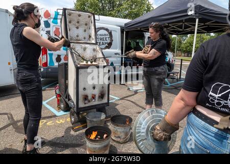 Detroit, Michigan - Mitglieder des Pewabic Pottery Street Teams demonstrieren die japanische Technik des Raku-Feuers von Töpferwaren auf einem Gemeinschaftskunstwerk und einem Mu Stockfoto