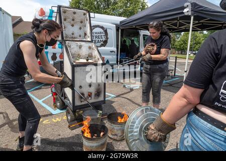 Detroit, Michigan - Mitglieder des Pewabic Pottery Street Teams demonstrieren die japanische Technik des Raku-Feuers von Töpferwaren auf einem Gemeinschaftskunstwerk und einem Mu Stockfoto