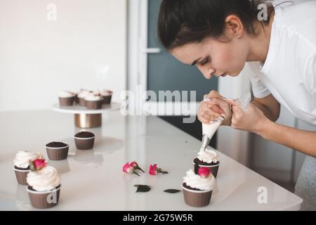 Frau schmücken hausgemachte cremige Schokolade Tasse Kuchen mit Creme Aufenthalt auf Küchentisch Nahaufnahme. Vorbereitung auf Geburtstag oder Hochzeitstag Stockfoto