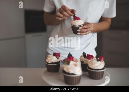 Frau schmücken cremige Schokolade Tasse Kuchen mit frischen Blumenrosen bleiben auf weißem Tablett in der Küche Nahaufnahme. Stockfoto