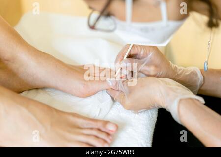 Kosmetikerin, die eine Pediküre malt, um die Nägel ihrer Kundin in einem Beauty-Center zu malen. Stockfoto