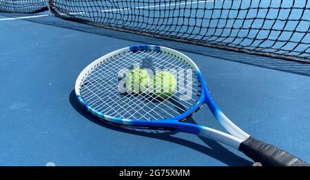 Horizontale Ansicht von zwei Tennisbällen mit einem Schläger oben auf einem blauen Tennisplatz. Stockfoto