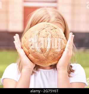 Das Kind hält ein rundes Brot. Gesunde Ernährung. Großes frisches Bäckerbrötchen tragen Stockfoto