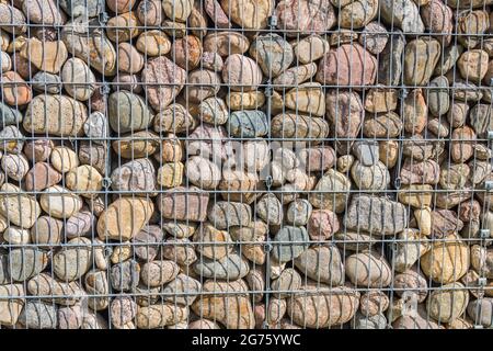 Gabionenzaun. Stein Wand Textur, Felsen hinter Metall Gitter Zaun Hintergrund. Stockfoto