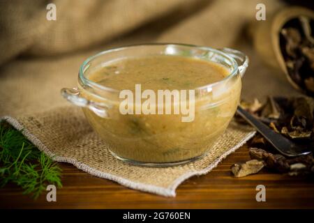 Heiße, hausgemachte vegetarische Gemüsesuppe mit getrockneten Pilzen in einer Glasschüssel auf einem Holztisch Stockfoto