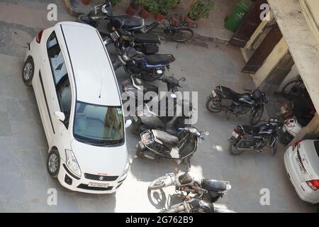 Draufsicht auf Auto- und Fahrradparkplätze in Indien. In der Sommersaison in City parken Fahrräder, Roller und Autos im Schatten. Zwei Leute reden.: Udaipur Stockfoto