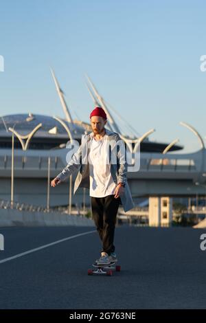 Modischer Hipster-Mann beim Schlittschuhlaufen auf Longboard im Freien. Bärtiger Tausendjähriger Kerl auf Skateboard im urbanen Raum Stockfoto