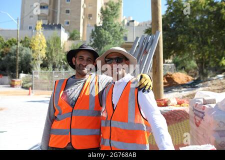 Ein ehrliches Porträt zweier palästinensischer arabischer Männer, die der Kamera zuschauen und lächeln, beide sind ausländische Straßenbauarbeiter, die Schutzwesten tragen. Stockfoto