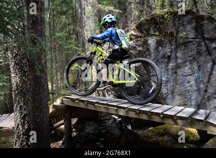 Banff Alberta Kanada, 7 2021. Juli: Ein kleiner Junge fährt mit dem Mountainbike eine Holzrampe entlang des erstklassigen Radweges am Tunnel Mountain. Stockfoto