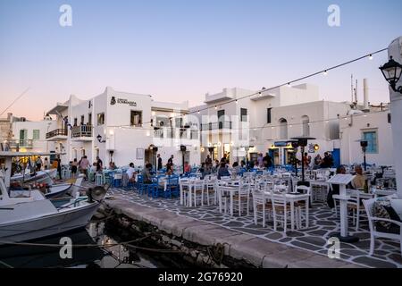 Griechenland, Paros Insel Naousa alten Hafen. 19.Mai 2021. Die Menschen speisen in traditionellen Fischtavernen im Freien, typische Fischerboote liegen am Hafendock Stockfoto