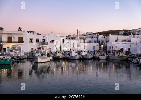 Griechenland, Paros Insel Naousa alten Hafen. 19.Mai 2021. Typische Fischerboote, die am Hafendock festgemacht sind, Menschen im traditionellen Café und Restaurant im Freien Stockfoto