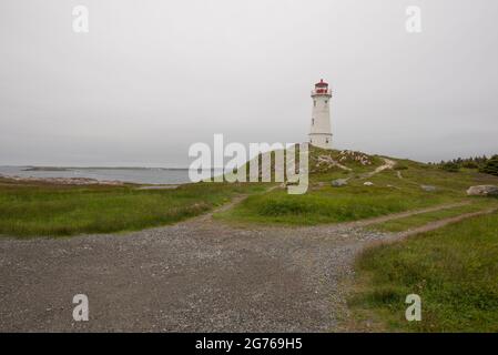 Louisbourg Leuchtturm mit Fortresse Louisbourg in der Ferne, gegenüber dem Hafen. Stockfoto