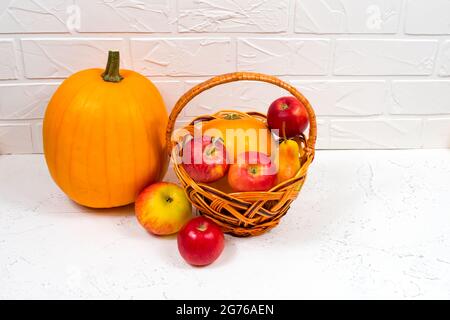 Orangefarbene Kürbisse mit Äpfeln und Birnen in einem Weidenkorb auf weißem Hintergrund. Stillleben im Herbst. Stockfoto