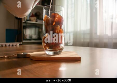 Ein erfrischendes Getränk zubereiten, indem Sie Eiswürfel aus Kaffee zubereiten und Milch in ein Glas gießen. Ein erfrischendes Getränk kalten Kaffee an einem Sommermorgen. Stockfoto