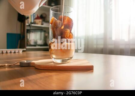 Ein erfrischendes Getränk zubereiten, indem Sie Eiswürfel aus Kaffee zubereiten und Milch in ein Glas gießen. Ein erfrischendes Getränk kalten Kaffee an einem Sommermorgen. Stockfoto