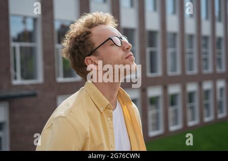 Junger nachdenklicher Mann mit geschlossenen Augen atmet frische Luft und entspannt sich im Park. Digitales Detox-Konzept Stockfoto