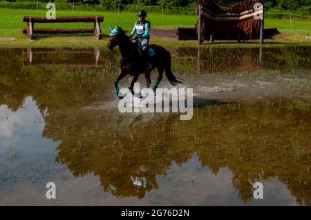 Raeford, North Carolina, USA. Juli 2021. BECCA SWAN reitet Delmonico und spritzt durch den Montrose Water Complex im Langlauf bei der war Horse Event Series 2021, Juli 11 im Carolina Horse Park in Raeford, N.C. Die 2013 als Cabin Branch Event Series gegründete war Horse Event Series besteht aus fünf Pferdeversuchen und kombinierten Tests und zieht Reiter und ihre Pferde aus dem gesamten Osten der Vereinigten Staaten an. Quelle: Timothy L. Hale/ZUMA Wire/Alamy Live News Stockfoto