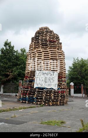 Das umstrittene Lagerfeuer an der Adam Street in der unionistischen Tiger's Bay Area steht in der Nähe einer Schnittstelle zur nationalistischen New Lodge und hat Kritik ausgelöst. Auf dem Lagerfeuer ist ein Transparent mit der Aufschrift „Loyalist Tigers Bay Bonfire“ angebracht. Die Vorbereitungen für die Lagerfeuernacht am 11. Juli in Belfast vor den jährlichen Märschen der Oranje Order vom 12. Juli laufen. In diesem Jahr jährt sich die Gründung Nordirlands zum hundertsten Mal und ist gleichzeitig der erste zugelassene Orangen-Marsch seit Beginn der Pandemie. Die Marschsaison ist in einer angespannten Zeit gefallen, in der die Brexit-Protokolle eine politische Debatte auslösen Stockfoto