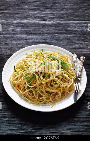 Sommer-Spaghetti alla carrettiera mit Minzblättern, Zitronenschale, Pecorino-Käse, Chilischoten-Flocken, Petersilie und geriebenen Zucchini auf einem weißen Teller Stockfoto