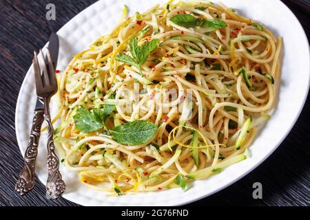 Sommer-Spaghetti alla carrettiera mit Minzblättern, Zitronenschale, Pecorino-Käse, Chilischoten-Flocken, Petersilie und geriebenen Zucchini auf einem weißen Teller Stockfoto