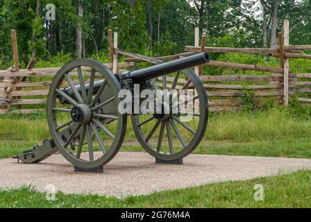 Gettysburg, PA, USA - 14. Juni 2008: Schlachtfelddenkmäler. Nahaufnahme einer Kanone mit glänzendem Fass auf braunem Beton mit Holzzaun und grünem Blatt Stockfoto